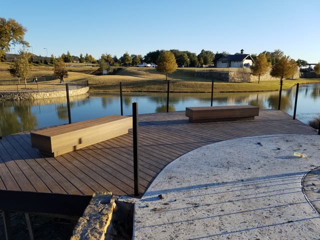 Composite dock deck at golden hour with two long built-in benches and black steel posts, overlooking a neighborhood pond.