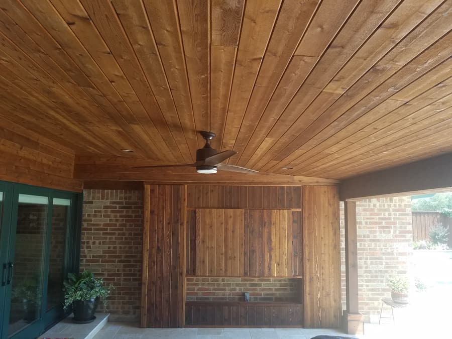 Covered patio with a stained cedar plank ceiling, dark ceiling fan and a vertical cedar accent wall built over existing brick.