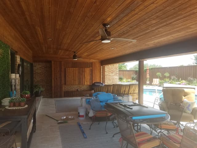 Large covered patio with a warm stained cedar tongue-and-groove ceiling, two ceiling fans and recessed lighting, opening onto a pool.