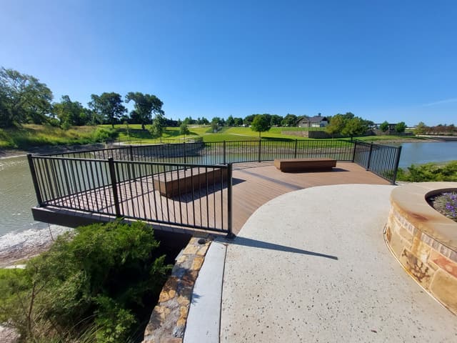 Finished composite overlook deck cantilevered over a lake, with steel railing, built-in benches and a curved stone fire pit.