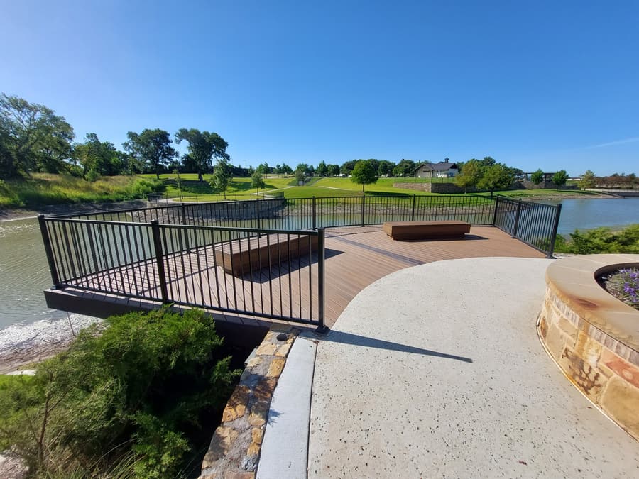 Finished composite overlook deck cantilevered over a lake, with steel railing, built-in benches and a curved stone fire pit.
