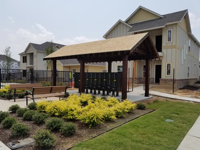 Timber-frame mail kiosk pavilion with stained posts and a gable roof, sheltering cluster mailboxes at a residential community.