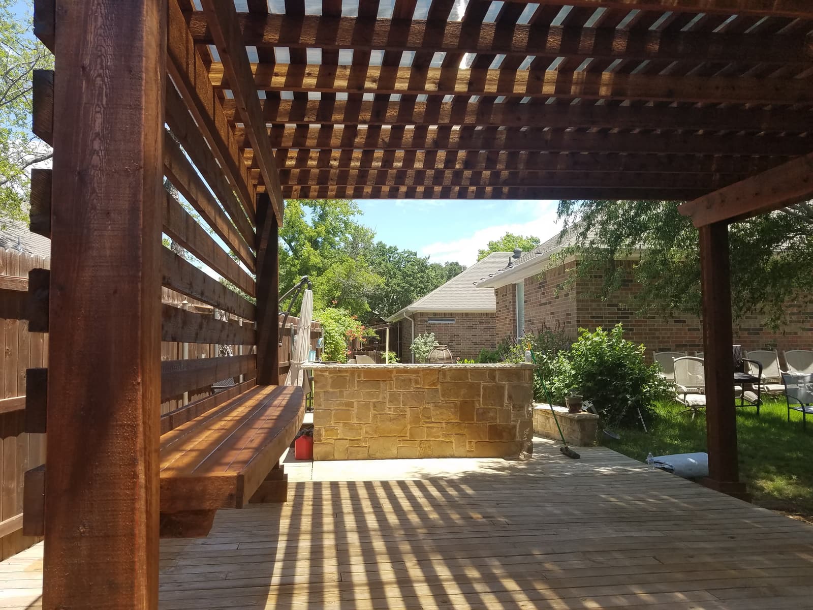 Cedar pergola over a wood deck with a horizontal-slat privacy screen, built-in bench seating and a stone outdoor bar.