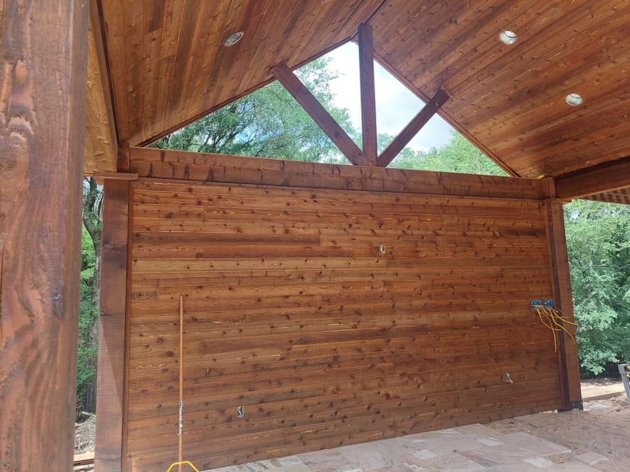 Interior of a vaulted cedar pavilion showing an exposed king-post truss, stained plank ceiling, recessed lighting and a horizontal cedar wall.